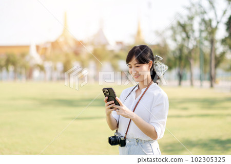 Portrait beautiful young asian woman with smartphone on summer holiday vacation trip with the grand palace in a background at Bangkok, Thailand Portrait beautiful young asian woman with smartphone on summer holiday vacation trip with the grand palace in a background at Bangkok, Thailand 102305325