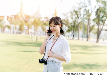 Portrait beautiful young asian woman with smartphone on summer holiday vacation trip with the grand palace in a background at Bangkok, Thailand Portrait beautiful young asian woman with smartphone on summer holiday vacation trip with the grand palace in a background at Bangkok, Thailand 102305326