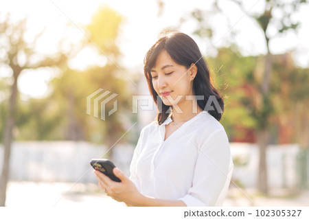 Portrait beautiful young asian woman with smart mobile phone around outdoor nature view in a sunny summer day Portrait beautiful young asian woman with smart mobile phone around outdoor nature view in a sunny summer day 102305327
