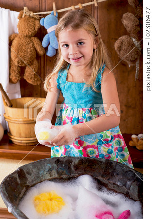 Fun home photo session. Curious little girl washes bears in an antique copper basin with water and soap suds at home 102306477