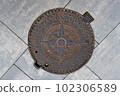 Metal manhole of heating main well with relief image of wind rose engraved on lid. On surface, you can see outline of four-pointed star and holes of vents. 102306589