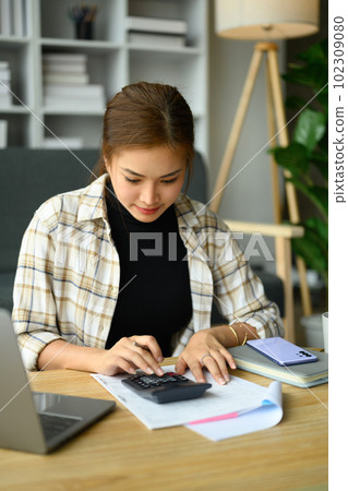 Focused asian woman calculating domestic expenses, utility bills at home. Finance management concept 102309080