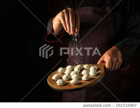 The chef adds salt to meat dumplings on a cutting board. Concept for a hotel menu on a black background with space for advertising 102310407
