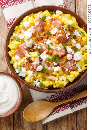 Typical Ukrainian dish polenta Banosh with onion, cracklings and cheese closeup on the bowl on the wooden table. Vertical top view 102310498