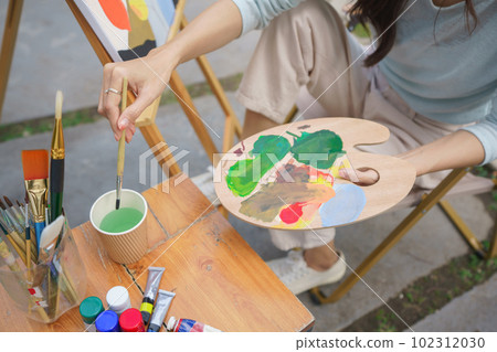 Creative art concept, Female artist is washing paintbrush while painting art on canvas in garden 102312030