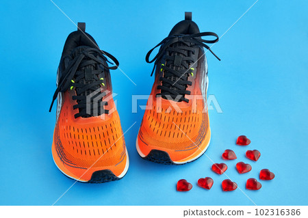 Orange running shoes and red decorative glass hearts scattered on a blue background Orange running shoes and red decorative glass hearts scattered on a blue background 102316386