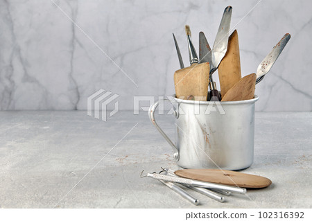 Variety of tools for sculpting and modeling in an aluminum cup and on a light stone background Variety of tools for sculpting and modeling in an aluminum cup and on a light stone background 102316392