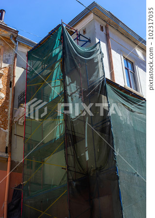 Restoration of the building. Scaffolding and protective green building mesh. Safety techniques during construction works 102317035