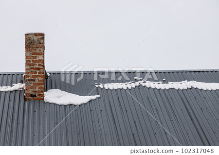 a brick chimney on a metal roof in the winter under the snow. construction concept 102317048