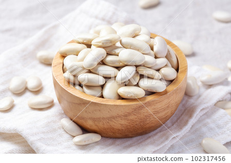 White beans in wood bowl with spoon on linen cloth, closeup White beans in wood bowl with spoon on linen cloth, closeup 102317456