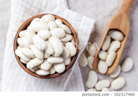 White beans in wood bowl with scoop on linen cloth background, top view 102317460