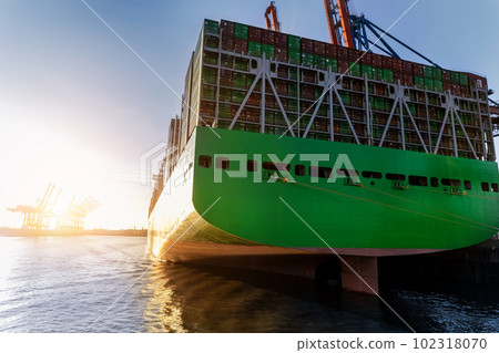 Scenic view giant cargo container ship loading Hamburg city port harbour against seaport cranes warm evening sunset lights. Global commercial trade freight charter shipping and logistics background Scenic view giant cargo container ship loading Hamburg city port harbour against seaport cranes warm evening sunset lights. Global commercial trade freight charter shipping and logistics background 102318070