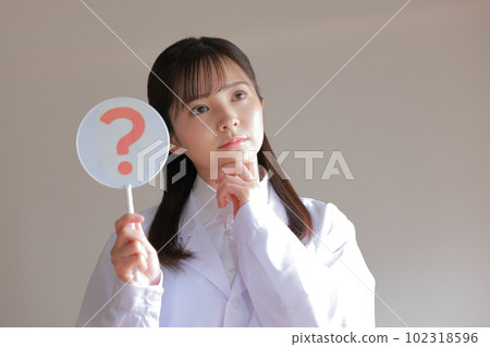 A woman in a white coat holding a Hatena plate and putting her hand on her chin _ looking away 1 102318596