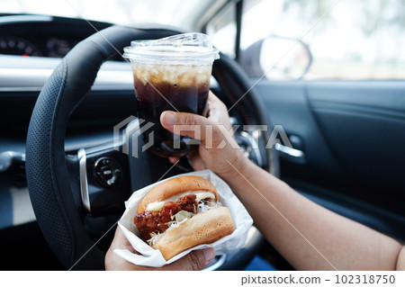 Asian woman driver hold and eat hamburger in car, dangerous and risk an accident. Asian woman driver hold and eat hamburger in car, dangerous and risk an accident. 102318750