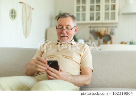 Happy middle aged senior man holding using smartphone touch screen typing scroll page. Stylish older mature beard grandfather with cell phone using internet social media apps at home. Shopping online Happy middle aged senior man holding using smartphone touch screen typing scroll page. Stylish older mature beard grandfather with cell phone using internet social media apps at home. Shopping online 102319804