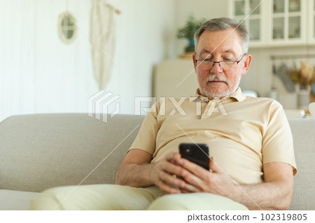 Happy middle aged senior man holding using smartphone touch screen typing scroll page. Stylish older mature beard grandfather with cell phone using internet social media apps at home. Shopping online Happy middle aged senior man holding using smartphone touch screen typing scroll page. Stylish older mature beard grandfather with cell phone using internet social media apps at home. Shopping online 102319805