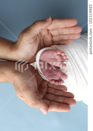 Tiny foot of a newborn baby. Soft legs of a newborn in a white blanket. Close up the toes, heels and feet of a newborn baby. Studio macro photography baby feet on a white background. 102319985
