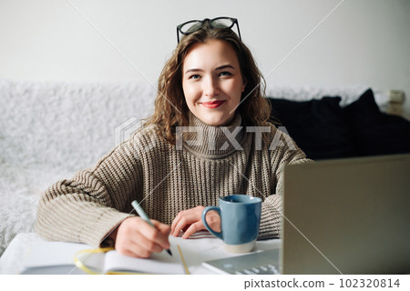 Home office of a young female English tutor with laptop, coffee, and notes, preparing for online 102320814