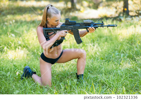 Caucasian woman in bikini sits with machine gun on green grass. Caucasian woman in bikini sits with machine gun on green grass. 102321336