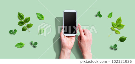 Person using a smartphone with green leaves 102321926