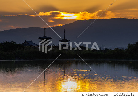 Yakushi-ji Temple in Nara, where the sky and the water surface of Oike shine in golden color and the morning sun covered with a veil of thin clouds is beautiful. 102322112