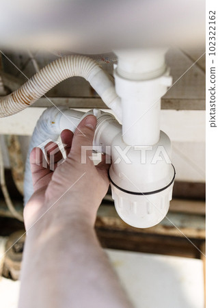 plumber's hand disassembles old plastic siphon 102322162