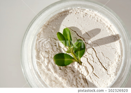 An open jar of facial scrub powder with a green sprig. An open jar of facial scrub powder with a green sprig. 102326920