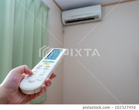 A woman's hand setting the temperature with the remote control of the air conditioner (setting 28°C, blower opening) 102327458
