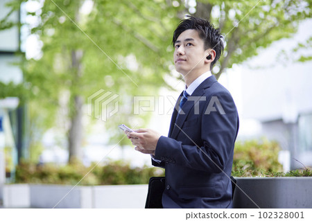 一名日本男性上班族正在使用無線耳機和智慧型手機 一名日本男性上班族正在使用無線耳機和智慧型手機 102328001