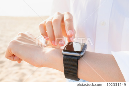 Woman hand wearing a smartwatch and checking active lifestyle and using fitness tracker outdoor. 102331249