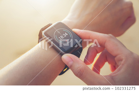 Woman hand wearing a smartwatch and checking active lifestyle and using fitness tracker outdoor. 102331275