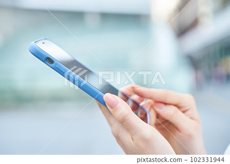 Hand of a woman using a smartphone on a street corner 102331944
