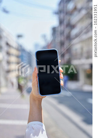 Hand of a woman using a smartphone on a street corner 102331951
