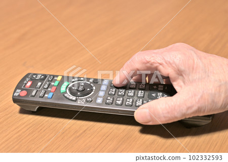 Elderly woman's fingertips operating the TV remote control 102332593