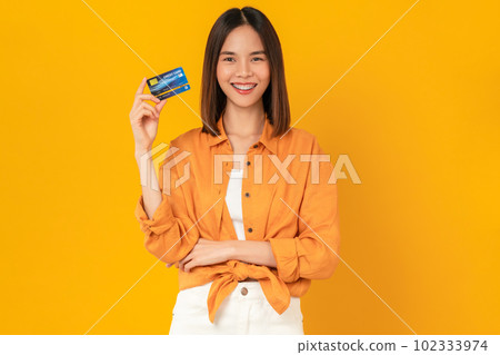Cheerful beautiful Asian woman holding mockup credit card on orange background. 102333974
