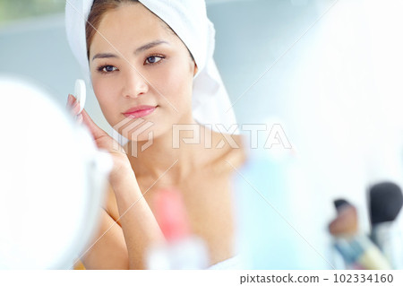 Maintaining her flawless beauty. An attactive young Asian woman applying moisturizer with a towel on her head. 102334160