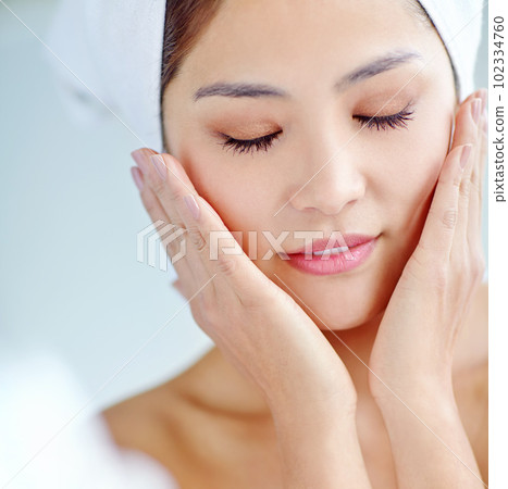 Naturally flawless. A beautiful young Asian woman touching cheeks while wearing a towel on her hand. Naturally flawless. A beautiful young Asian woman touching cheeks while wearing a towel on her hand. 102334760