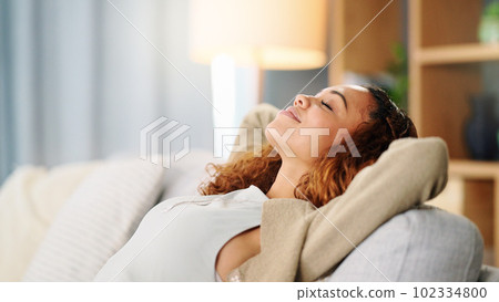 Woman, relax and hands behind head on sofa, living room and lounge for happiness, calm mind and easy lifestyle at home. Happy young female in peace on couch, smile and zen mental health for self care 102334800