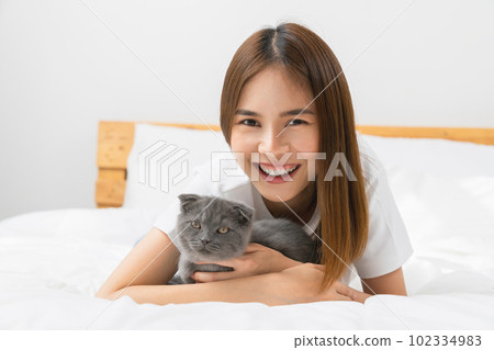Young Asian woman lying on bed and playing small Scottish kitten on the room. Young Asian woman lying on bed and playing small Scottish kitten on the room. 102334983