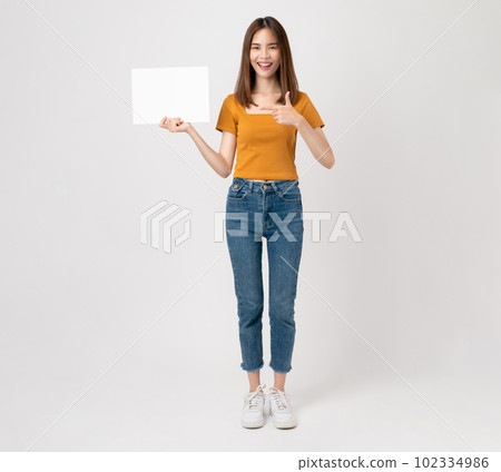 Happy young Asian woman holding a blank paper with smiling face and looking at the pink background. Happy young Asian woman holding a blank paper with smiling face and looking at the pink background. 102334986