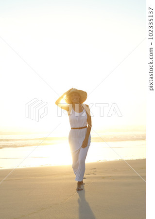 Shes a vision in white. a gorgeous young woman in a hat and white dress walking on a beach. Shes a vision in white. a gorgeous young woman in a hat and white dress walking on a beach. 102335137