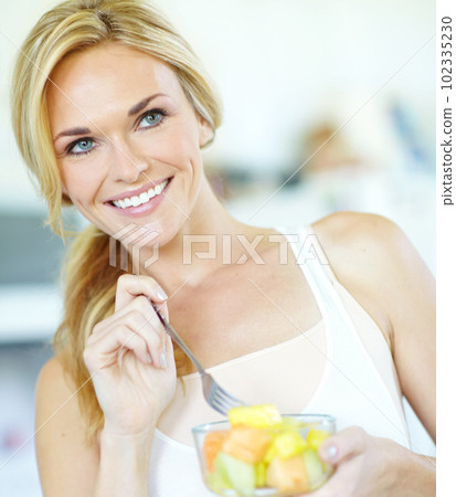 Fresh fruit salad is the best. Attractive young blonde woman enjoying a delicious fresh fruit salad at home. 102335230