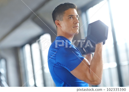 Training to hold up the world. a handsome young man lifting dumbells in a gym. Training to hold up the world. a handsome young man lifting dumbells in a gym. 102335390