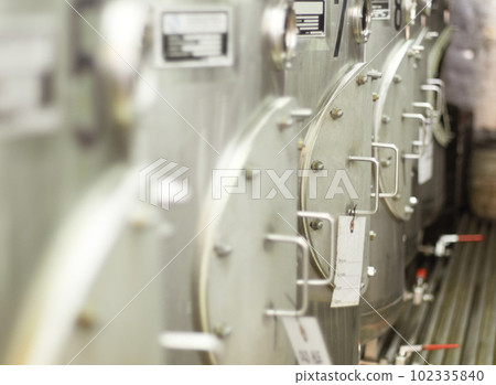 Closeup, stainless steel and fermentation tanks for brewing beer at a breweries, factory or warehouse. Alcohol, machine and barrel at a manufacturing plant for process, fermentation and procedure 102335840