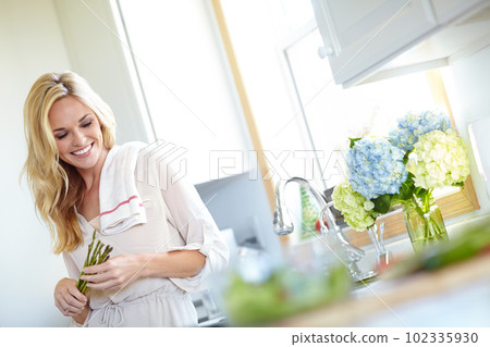 Planning a meal with this asparagus. Attractive blonde woman holding asparagus in her kitchen at home. 102335930