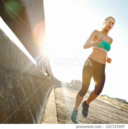 Keeping a steady pace. an attractive young woman out on her morning run. 102335997