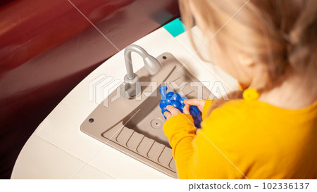 child in kindergarten, playroom, playing with toys, learning. plays in kitchen, cooks vegetables and fruits. washes grapes under tap child in kindergarten, playroom, playing with toys, learning. plays in kitchen, cooks vegetables and fruits. washes grapes under tap 102336137