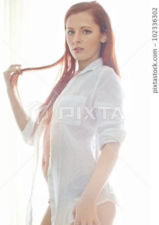 Shes a firery beauty. Portrait of an attractive redheaded woman wearing an unbuttoned shirt standing in a bedroom looking sexy while standing in her underwear. Young female posing semi nude. Shes a firery beauty. Portrait of an attractive redheaded woman wearing an unbuttoned shirt standing in a bedroom looking sexy while standing in her underwear. Young female posing semi nude. 102336302