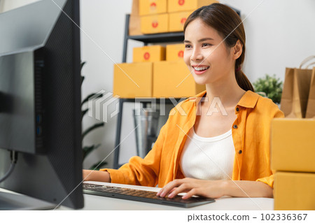 Asian woman checking online order on computer and packing boxes for products to send to customers Asian woman checking online order on computer and packing boxes for products to send to customers 102336367