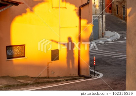 Shadow of a pointing man on an orange wall in the village of Cossignano in Italy. 102336539